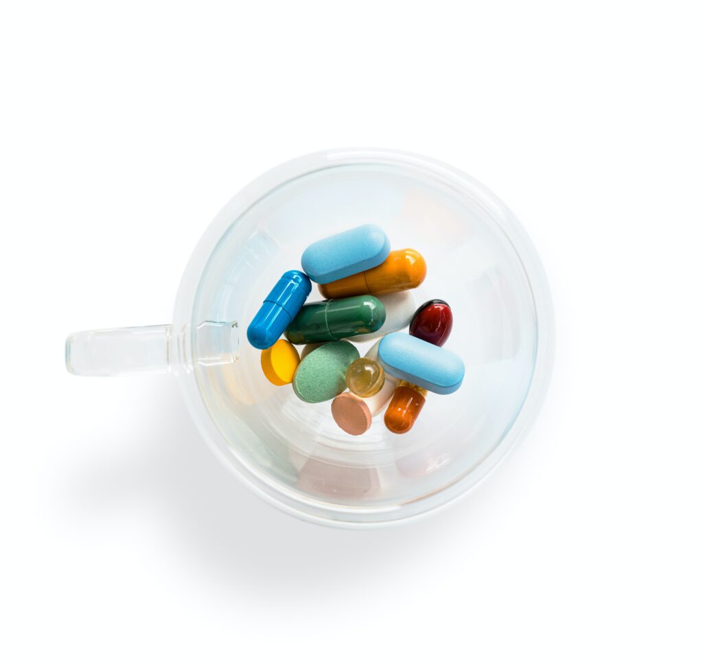 Different coloured pills in a plastic cup on a white background