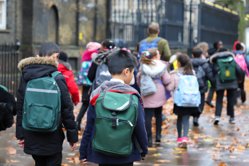 A group of school children walking on a wet street, wearing winter coats and backpacks.