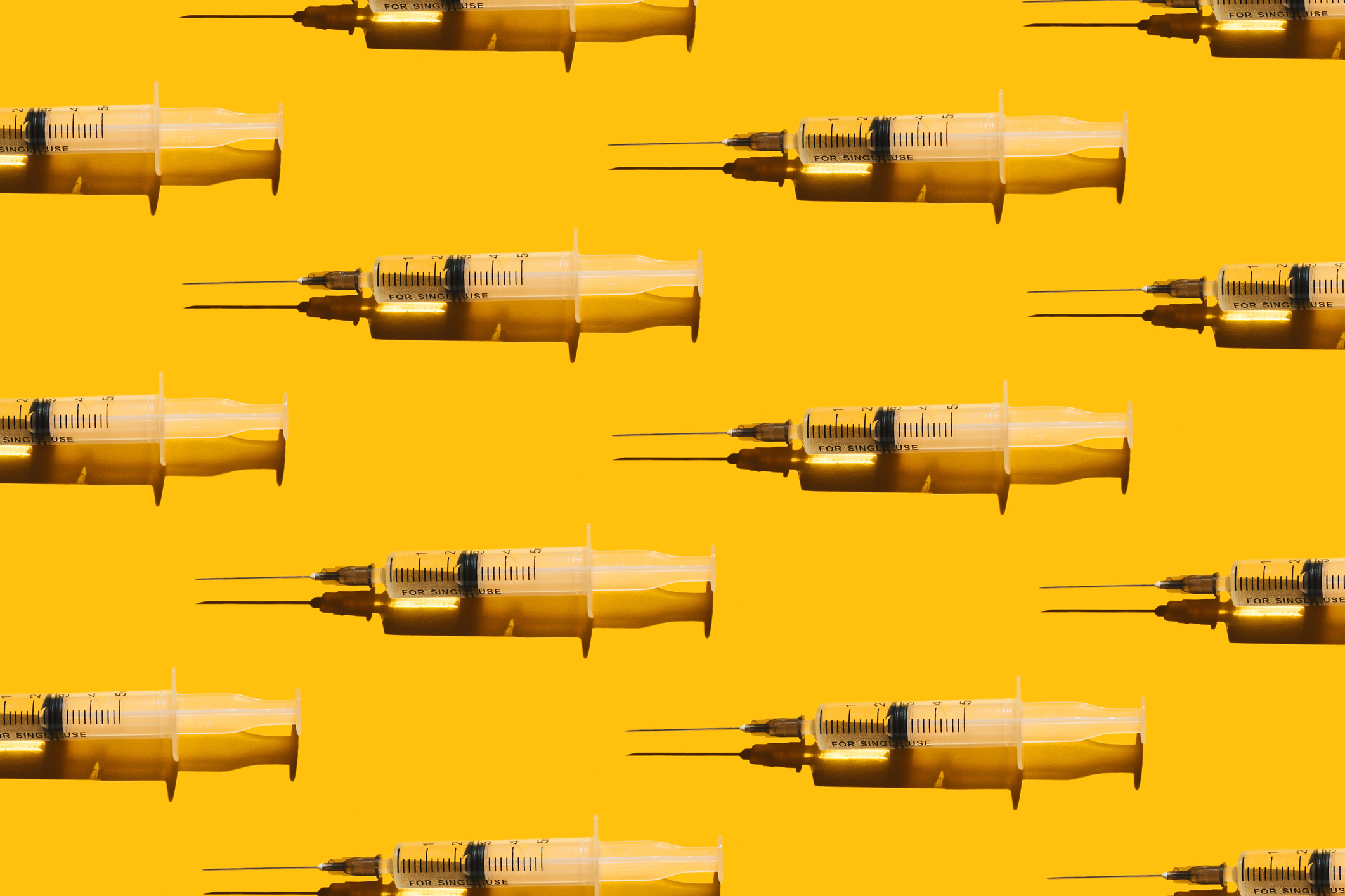 Pattern of syringes with a vaccine on yellow background. Concept of medical treatment or vaccination.