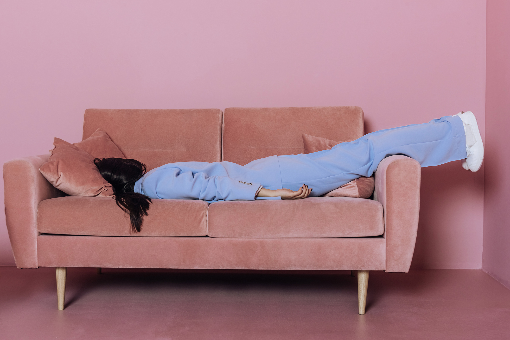 A woman lying in a blue suit on a pink sofa. 